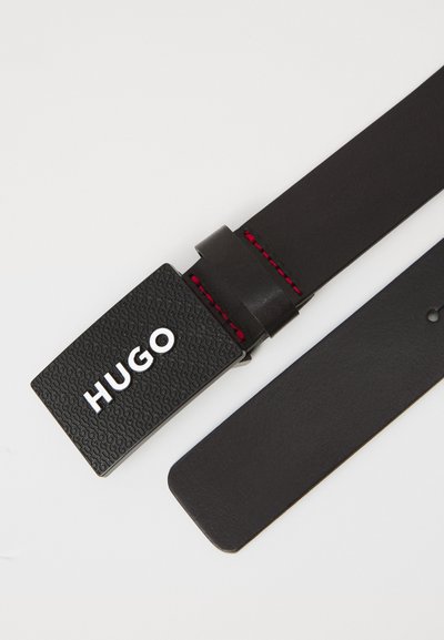 Ceinture en cuir noir avec une boucle rectangulaire texturée comportant "HUGO" en argent. Des coutures rouges ornent la zone de la boucle. Design de sangle lisse.