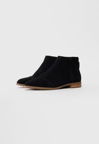 Botine din suede negre, cu toc jos maro, vârf rotund și cusături subtile, prezentate una lângă alta pe un fundal alb.
