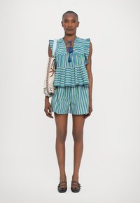 Top peplum a strisce blu e verdi con maniche arricciate abbinato a pantaloni corti coordinati. Ulteriore dettaglio include una borsa a tracolla con motivo.