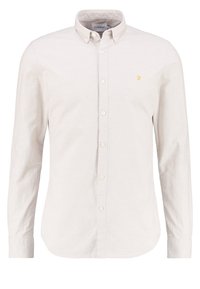 Camisa blanca de botonadura delantera hecha de tela texturizada. Mangas largas, cuello clásico y un pequeño logo amarillo en el pecho.