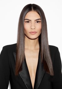 Blazer noir avec revers en satin, décolleté en V profond, et cheveux raides coiffés de manière lisse, mettant en valeur un teint lisse et un maquillage neutre.