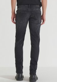 Jeans de mezclilla negra con corte ajustado, que cuentan con bolsillos traseros y un acabado ligeramente deslavado. Combinados con botas negras de tobillo.