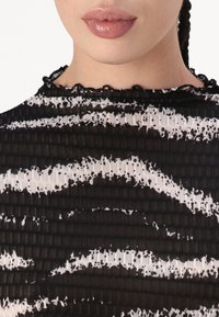 Černobílý vzorovaný top s texturovanou tkaninou, která má volánkový výstřih a těsně přiléhající design.