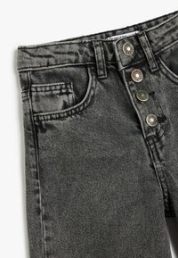 Jean noir en denim avec une taille haute, dotés d'une fermeture à cinq boutons, de poches avant et d'une texture légèrement dégradée sur le tissu.