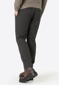 Dunkelgraue Hose mit strukturiertem Finish, schlanker Schnitt und seitlichen Taschen. Kombiniert mit braunen Wanderstiefeln mit robustem Profil.
