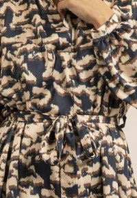 Robe imprimée en bleu marine, beige et marron. Dotée d'un col en V, de manches longues et d'une ceinture à la taille. Fabriquée en tissu lisse avec une texture fluide.