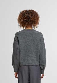 Grauer Strickpullover mit cropped Passform, überschnittenen Schultern und geripptem Saum, mit einer weichen, strukturierten Oberfläche. Lange, lockere Ärmel.