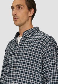 Blauw-wit geblokt overhemd met knopen, zachte textuur, kraagontwerp en subtiele groene accenten in het patroon.