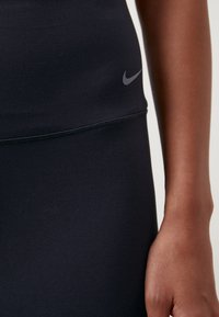 Czarny, sportowy top bez rękawów wykonany z gładkiego, elastycznego materiału. Posiada małe, szare logo Nike na klatce piersiowej oraz dopasowany krój.