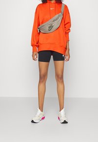 Orange hoodie med ett Nike-logotyp, svarta cykelshorts, grå axelbag och flerfärgade sneakers med rosa detaljer.
