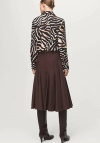 Bluza z vzorcem zebre z dolgimi rokavi, kombinirana s rjavo razširjeno krilo, dopolnjena z rjavimi usnjenimi škornji do kolen.