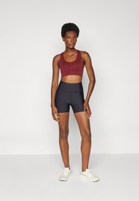 Completo sportivo composto da un reggiseno sportivo vino cropped e pantaloni corti neri a vita alta, completato da scarpe da ginnastica bianche. Tessuto dalla texture liscia.