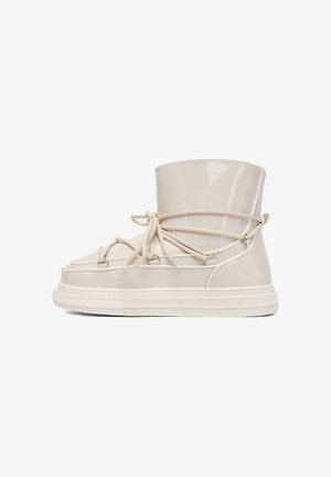 Krémově lakované kožené kotníkové boty s kulatou špičkou, předním šněrováním a silnou bílou gumovou podrážkou. Hladký povrch a minimalistický design.