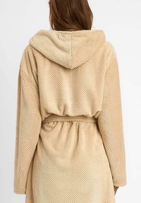 Beżowy szlafrok z teksturą, z kapturem, w pasie ze ściągaczem i długimi rękawami. Materiał jest miękki i przyjemny w dotyku.