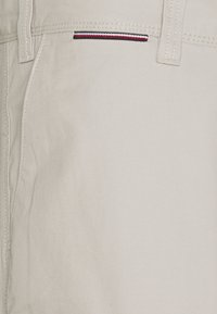 Pantalones de algodón beige con una textura suave, que cuentan con un pequeño bolsillo decorado con detalles a rayas en rojo, blanco y azul.