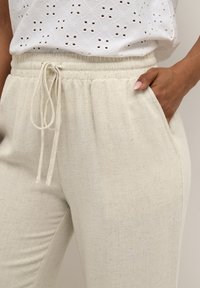 Pantaloni din in bej, ușori, cu un brâu elastic, șnur de strângere și buzunare laterale. Textură simplă cu un finisaj subtil, natural.