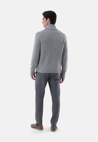 Grauer Strickpullover mit hochgeschlossenem Kragen, geripptem Saum, kombiniert mit grauen gemusterten Hosen und grauen Schuhen. Glatte Textur, lässige Passform.