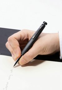 Musta metallikynä pidetään kädessä ja kirjoitetaan vaalealle paperille, josta näkyy teksti. Kynässä on tyylikäs muotoilu ja kiiltävä klipsi.