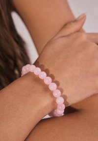 Rosa Perlenarmband aus glatten, glänzenden Perlen, das an einem Handgelenk getragen wird; zeichnet sich durch eine gleichmäßige runde Form und zarte Farbvariationen aus.