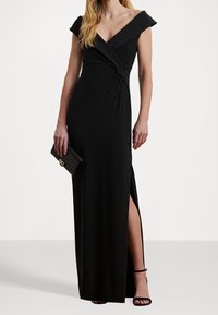 Abito nero lungo fino ai piedi con scollo a V, dettaglio vita intrecciata, maniche scese sulle spalle e una coscia alta per un movimento aggiuntivo.