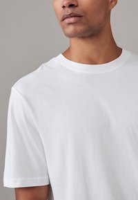 Fehér rövid ujjú póló puha anyagból, kör alakú nyakkivágással és normál szabással, sima textúrával, mintázat nélkül.