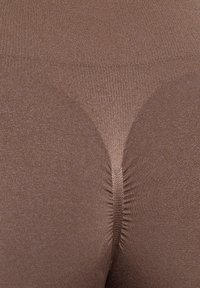 Brune sømløse strømpebukser med en glat, tekstureret overflade og en central kile-søm for komfort og pasform. Letvægts og elastisk materiale.