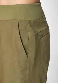 Olijfgroene broek met een brede, elastische tailleband. De stof heeft een gladde textuur met schuine voorzakken en gestikte naden.