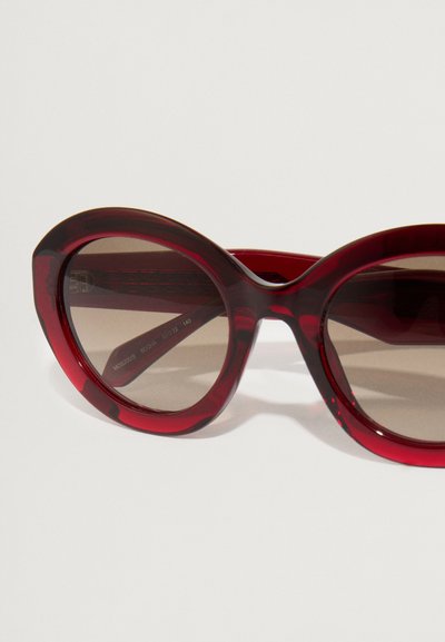 Punased, ülekaalulised prillid ümmarguse kassinäoga. Valmistatud läikivast plastmassist, gradient pruuni objektiiviga. Relvadel tekstuurilised detailid.