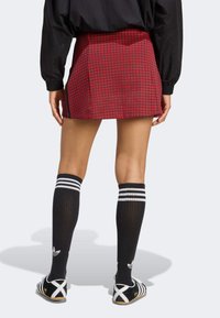 Red mini skirt with a houndstooth pattern, black knee-high socks with white stripes, and black shoes with a white sole.