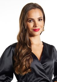 Musta satiiniwrap-mekko, jossa on syvä V-pääntie, puffihihat ja sileä pinta. Pitkät, laineikkaat hiukset ja kultaiset renkaat korvissa täydentävät asun.