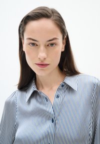 Randig skjorta med knappar i marinblått och vitt, med krage och två synliga knappar. Slät tygtextur och avslappnad passform.