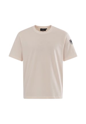 Camiseta beige de manga corta con cuello redondo, con un pequeño parche en blanco y negro en la manga izquierda y una etiqueta de la marca dentro del cuello.