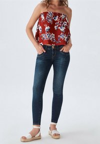 Top rojo floral sin mangas con un corte holgado, combinado con jeans ajustados azul oscuro. Sandalias de esparto blancas completan el conjunto.
