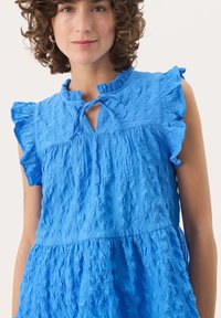 Helles blaues, strukturiertes Kleid mit Rüschensleeven, einem runden Ausschnitt und einem kleinen Schlüssellochausschnitt. Weicher, gekräuselter Stoff verleiht Tiefe und Interesse.