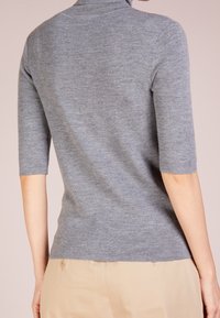 Suéter gris de manga corta con un diseño ajustado, textura acanalada y cuello alto, combinado con pantalones beiges que cuentan con detalles de botones.