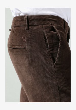 Pantaloni in corduroy marroni con texture a righe, passanti per cintura e una tasca posteriore con un piccolo logo. Vestibilità standard, con dettagli cuciti.