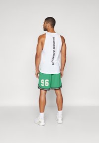Balta bez piedurknēm tank top krekls ar uzrakstu "UNDER ARMOUR" vertikāli uz muguras, saskaņots ar zaļiem sieta basketbola šortiem, kuros ir numurs "96."