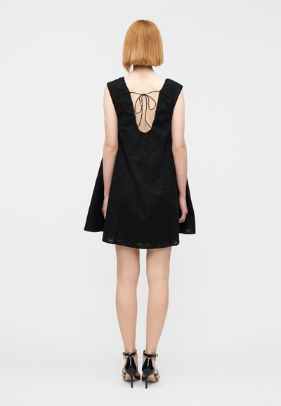 Μαύρο φόρεμα με φουσκωτή σιλουέτα, σχέδιο με οπές και ανοιχτή πλάτη στερεωμένη με κορδόνι. Συνδυασμένο με μαύρα ψηλά πέδιλα με ανοιχτές μύτες.