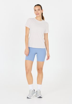 Let, kortærmet hvid t-shirt kombineret med blå tætsiddende shorts og grå træningssko; bomuldsagtig struktur, ingen mønstre eller accenter synlige.