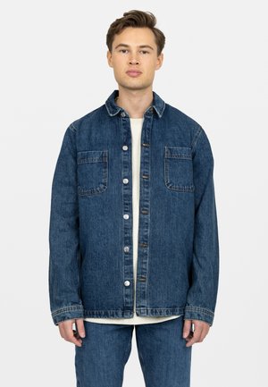 Denimjack in medium blauw met knoopsluiting, twee borstzakken en een klassieke kraag. Beschikt over een ontspannen pasvorm en contrasterende stitching.