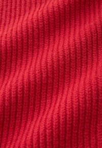Röd ribbad tyg med en texturerad yta, med vertikala ränder. Mjukt och flexibelt material, lämpligt för kläder eller möbelklädsel.