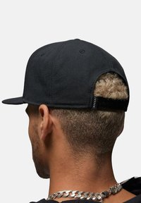 Sort baseballcap med flad skygge, lavet af tekstureret stof. Har en justerbar rem bagpå og subtile brandingdetaljer.
