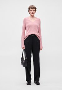 Ροζ ριμπ με ένα V-λαιμό, συνδυασμένο με ψηλόμεσα μαύρα παντελόνια. Τα αξεσουάρ περιλαμβάνουν μια μαύρη τσάντα και γυαλιστερά μαύρα παπούτσια.