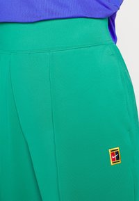 Pantalones deportivos verdes con una textura suave, cinturilla elástica y un pequeño logotipo multicolor de Nike en el lateral.
