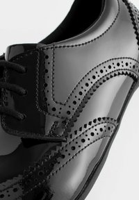 Zwarte gepolijste lederen schoen met brogue-afwerking, vetersluiting en een gladde glanzende textuur. Bevat geperforeerde accenten en zadelsteek.