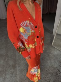 Cardigã laranja tricotado com padrões florais vibrantes de várias cores e botões. Combinado com uma saia laranja correspondente que apresenta motivos semelhantes.