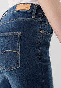 Vaqueros de mezclilla azul oscuro con una cintura de media altura, que presentan una etiqueta de cuero, detalles de costura sutiles y un diseño de bolsillo trasero.