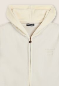 Felpa crema con zip realizzata in tessuto morbido. Presenta un cappuccio peloso, leggeri ricami con testo e una zip in metallo con una delle tirate a forma di cuore.