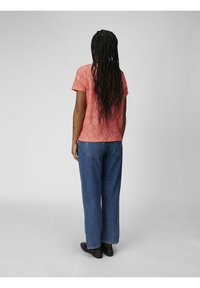 Haut en dentelle corail à manches courtes, avec un design en découpes florales, associé à un jean bleu taille haute et des chaussures noires.