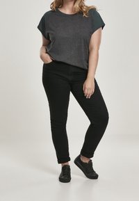 Top gris oscuro de manga corta con acentos en verde oscuro en los hombros, combinado con jeans negros de corte slim y zapatillas negras.